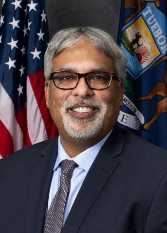 man in dark suit with American flag in background